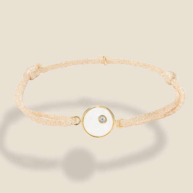 Bracelet ajustable, cordon beige pailleté, plaque ronde en plaqué or intérieur Nacre. Bijou seul, Crédit Léo Sédim