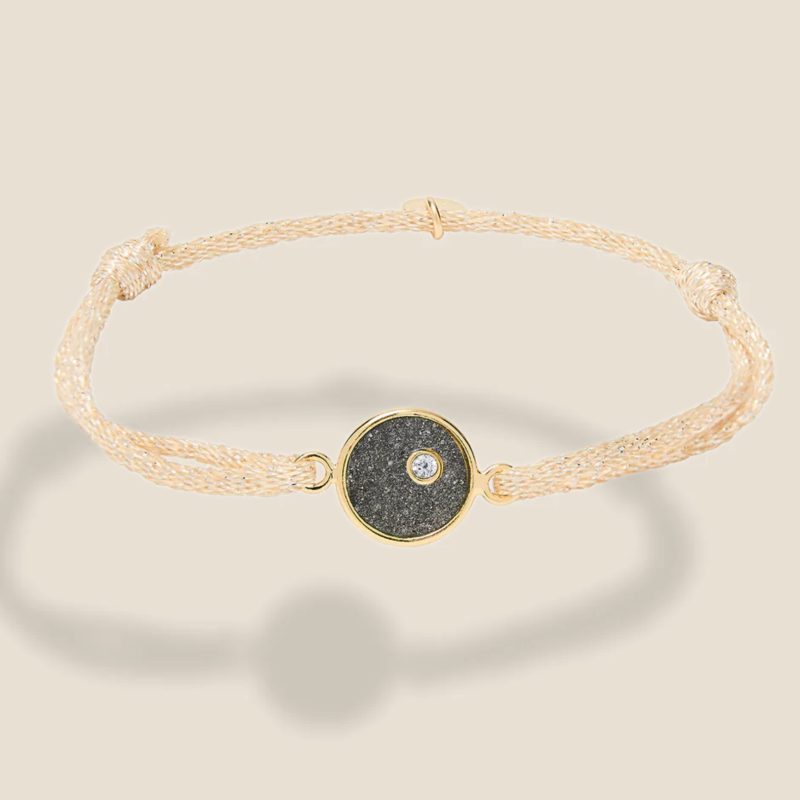 Bracelet ajustable, cordon beige pailleté, plaque ronde en plaqué or intérieur Pyrite. Bijou seul, Crédit Léo Sédim
