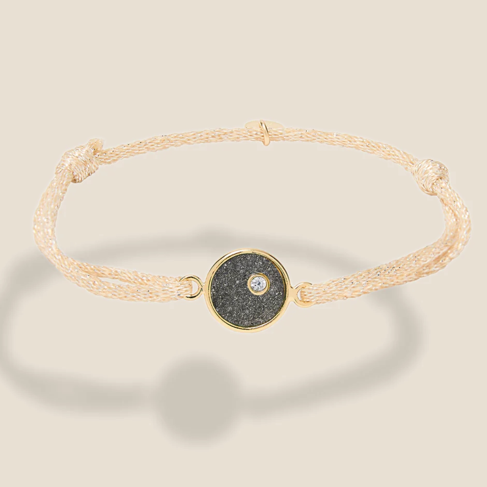 Bracelet ajustable, cordon beige pailleté, plaque ronde en plaqué or intérieur Pyrite. Bijou seul, Crédit Léo Sédim