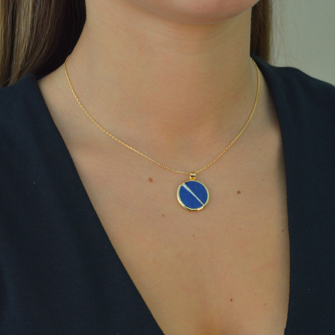 Collier plaquée or avec pendentif rond intérieur en lapis lazuli (bleu) avec un trait esthétique brillant dans son diamètre. Bijou porté, Crédit GEMITY.