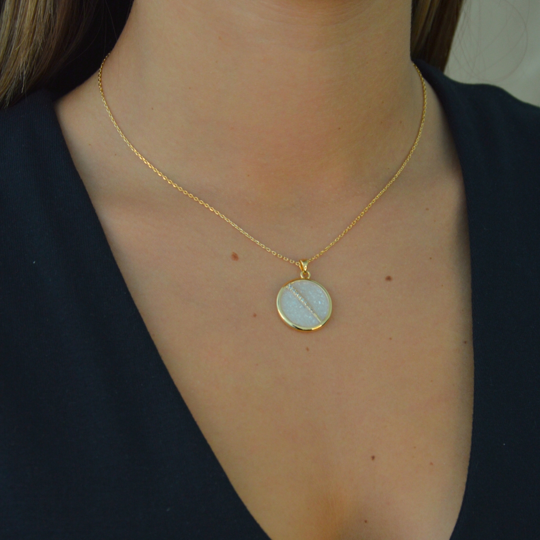 Collier plaquée or avec pendentif rond intérieur en nacre (blanc) avec un trait esthétique brillant dans son diamètre. Bijou porté, Crédit GEMITY.