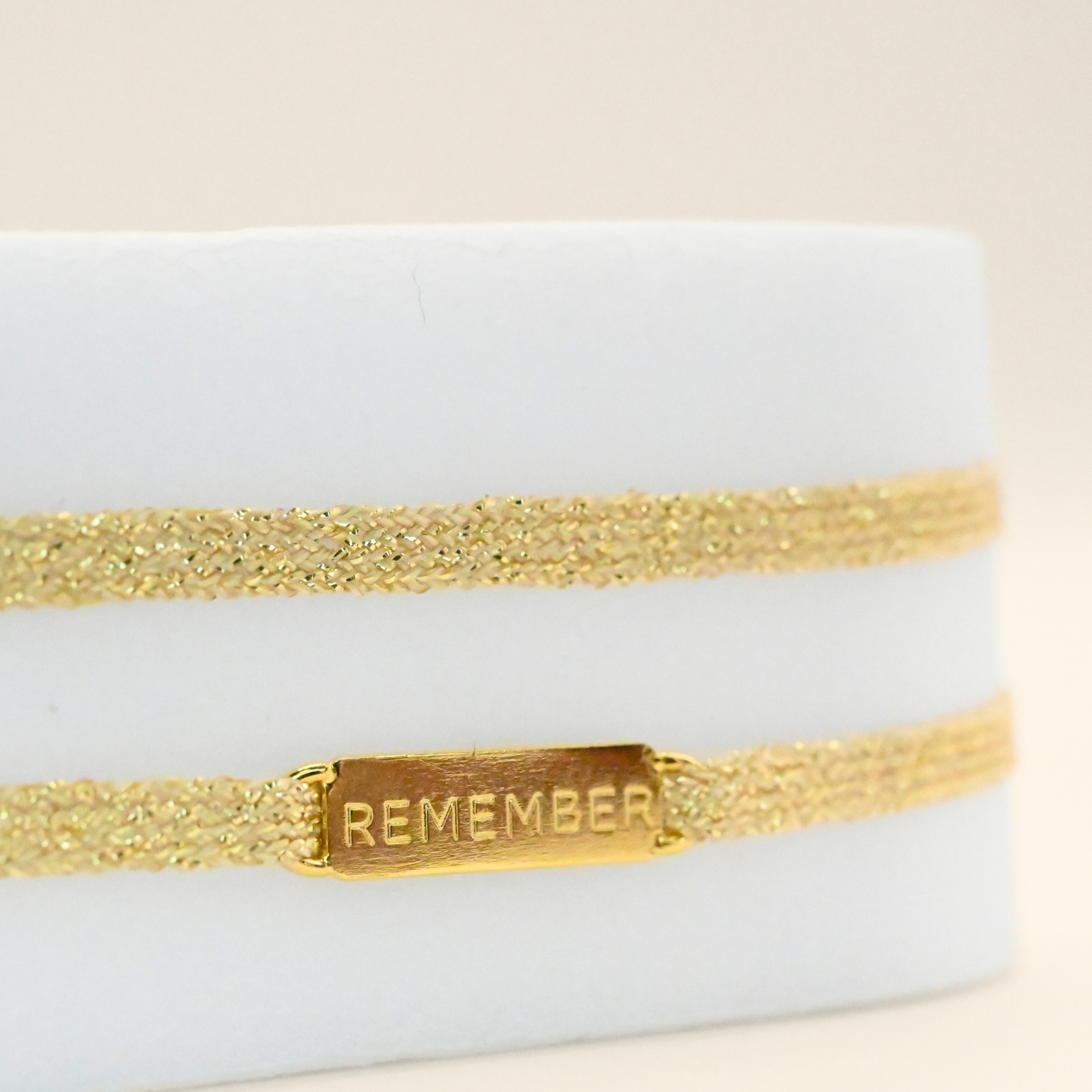 "Bracelet double tours en tissu avec une plaque REMEMBER en plaqué or (3 microns) fait main. Fermoir en plaqué or réglable . Bijou seul, Crédit GEMITY"