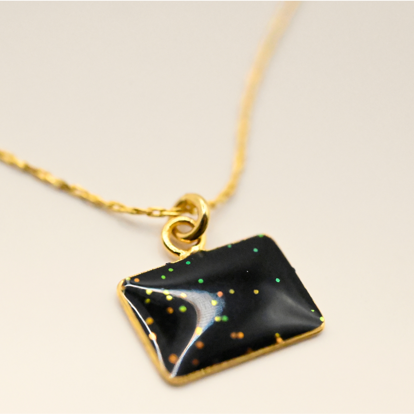 Collier plaqué or avec plaque extra-fine réversible, inscription LOVE d'un côté et émail noir pailleté de l'autre côté. Bijou seul, Crédit GEMITY