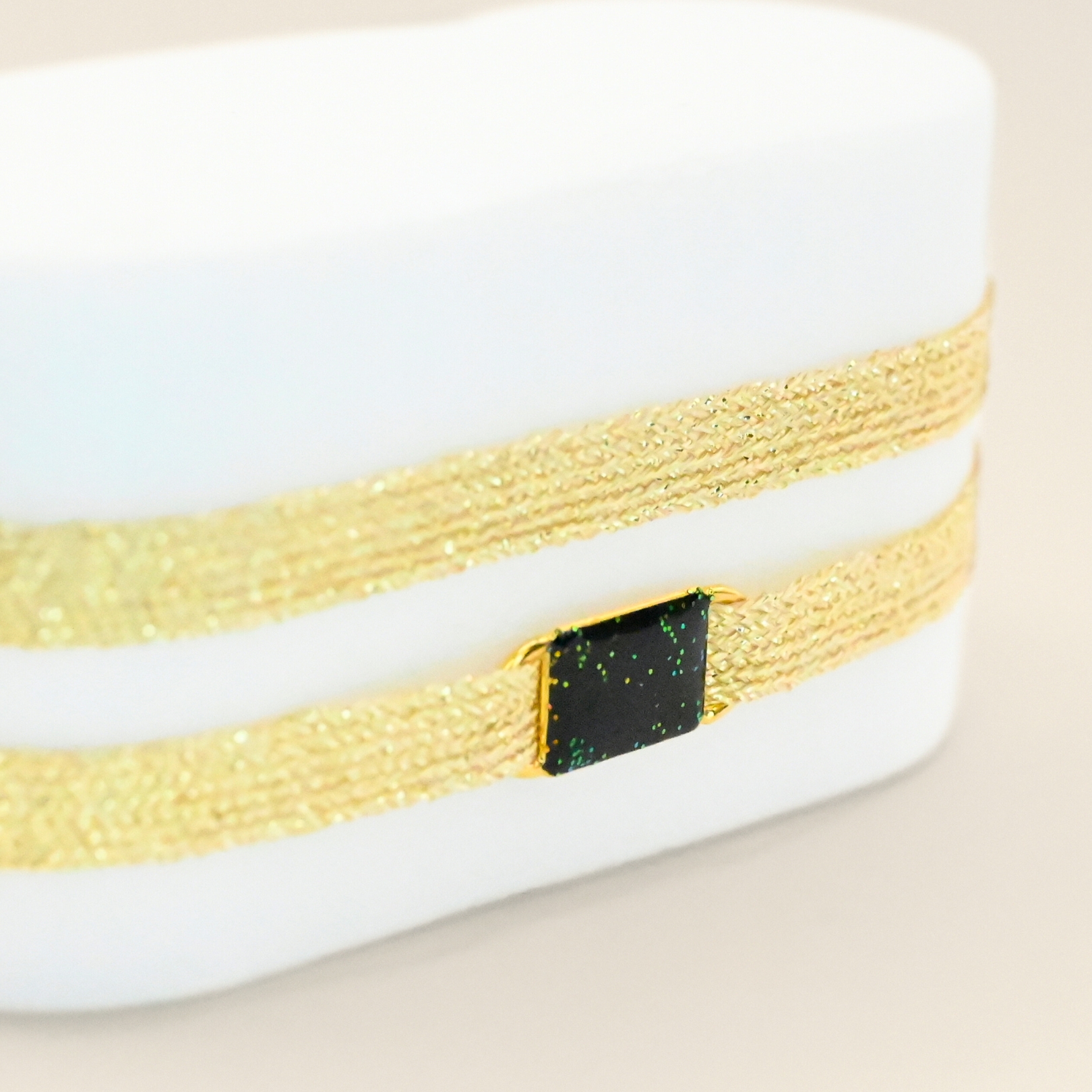"Bracelet double tours en tissu avec une plaque noire pailleté en plaqué or (3 microns) fait main. Fermoir en plaqué or réglable . Bijou seul, Crédit GEMITY"