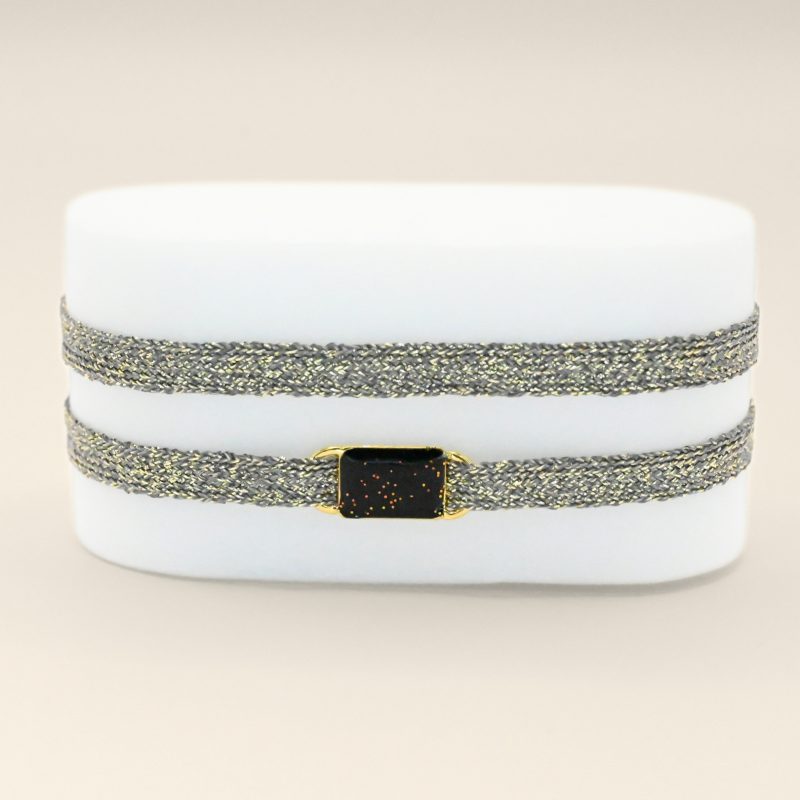 "Bracelet double tours en tissu avec une plaque noire pailleté en plaqué or (3 microns) fait main. Fermoir en plaqué or réglable . Bijou porté, Crédit GEMITY."