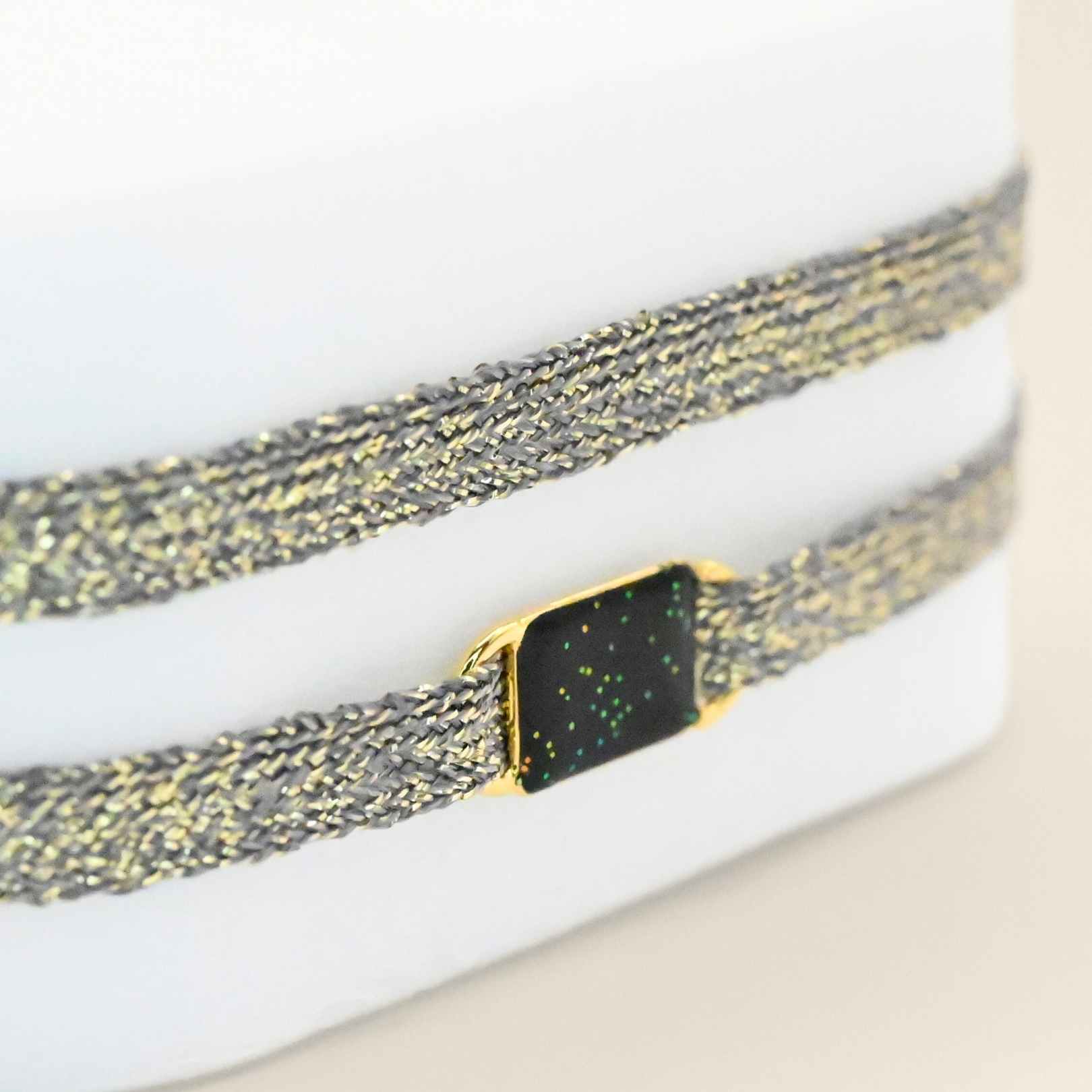 "Bracelet double tours en tissu avec une plaque noire pailleté en plaqué or (3 microns) fait main. Fermoir en plaqué or réglable . Bijou porté, Crédit GEMITY."