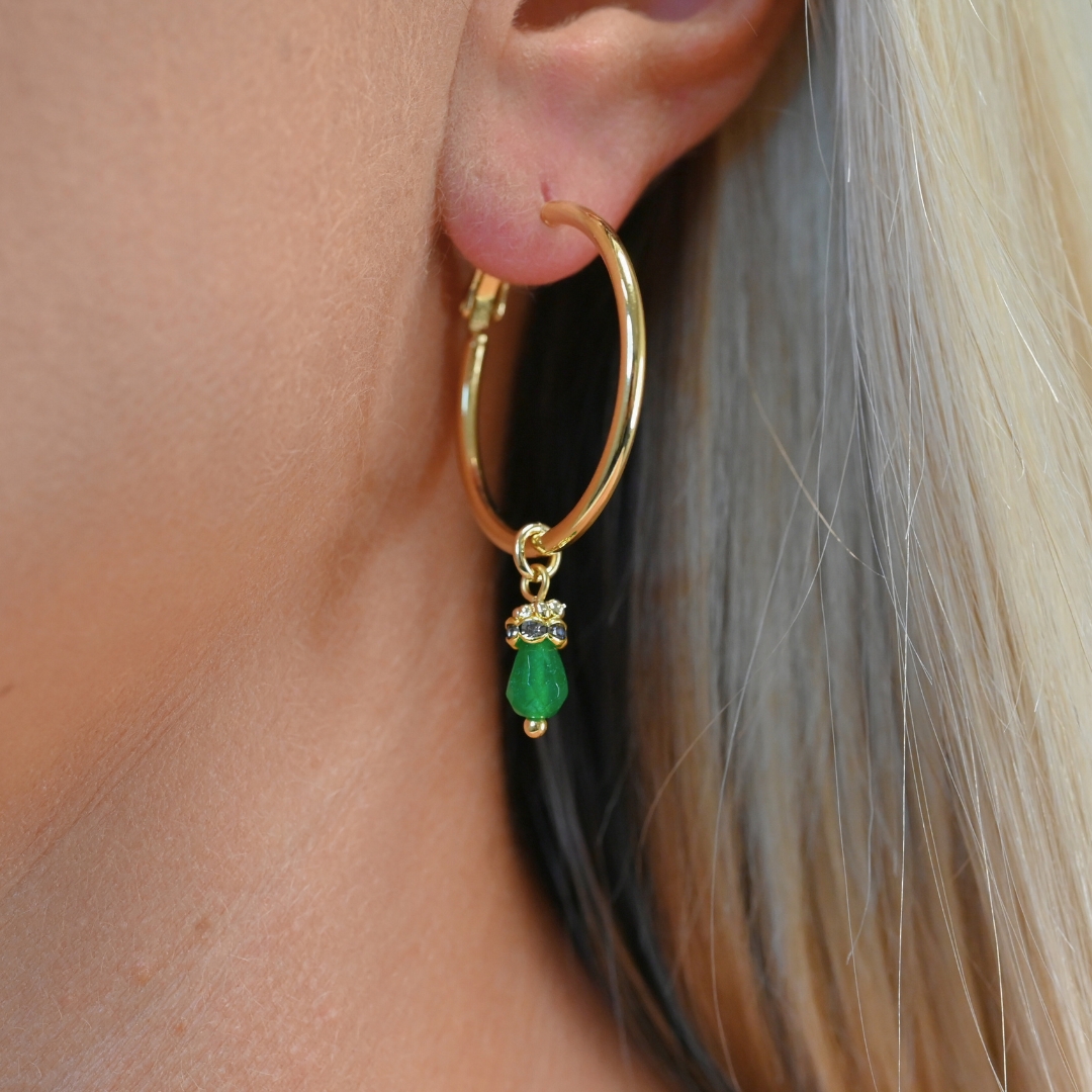 Découvrez l’élégance intemporelle de cette créole doré à l’or fin, ornée d’un délicat pendentif en pierre de jade teinté. Ces boucles d’oreilles allient sophistication et modernité, parfaites pour sublimer toutes vos tenues, qu’elles soient décontractées ou habillées. Bijou porté, Crédit GEMITY.