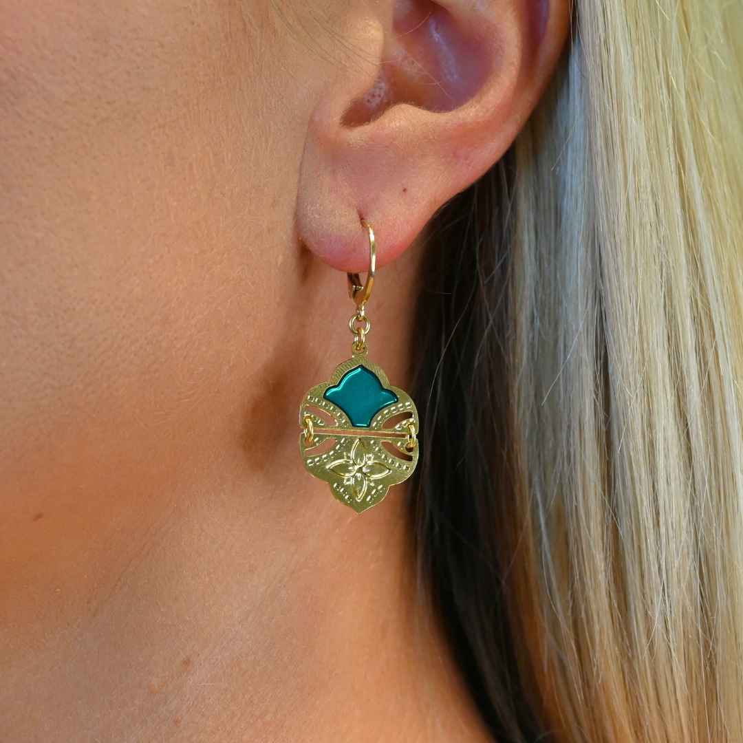 Comme un hommage aux volutes de l'architecture et palais indiens, ces boucles d’oreilles tout en courbes sublimeront votre visage. Elles sont émaillées de résine colorée transparente qui donne de la profondeur à la boucle. Elles sont en 2 parties pour plus de fluidité et de légèreté. La partie inférieure est gravée d'une fleur à 4 pétales. D'un style bohème chic, ce joli modèle vous accompagnera partout. Bijou porté, Crédit GEMITY.