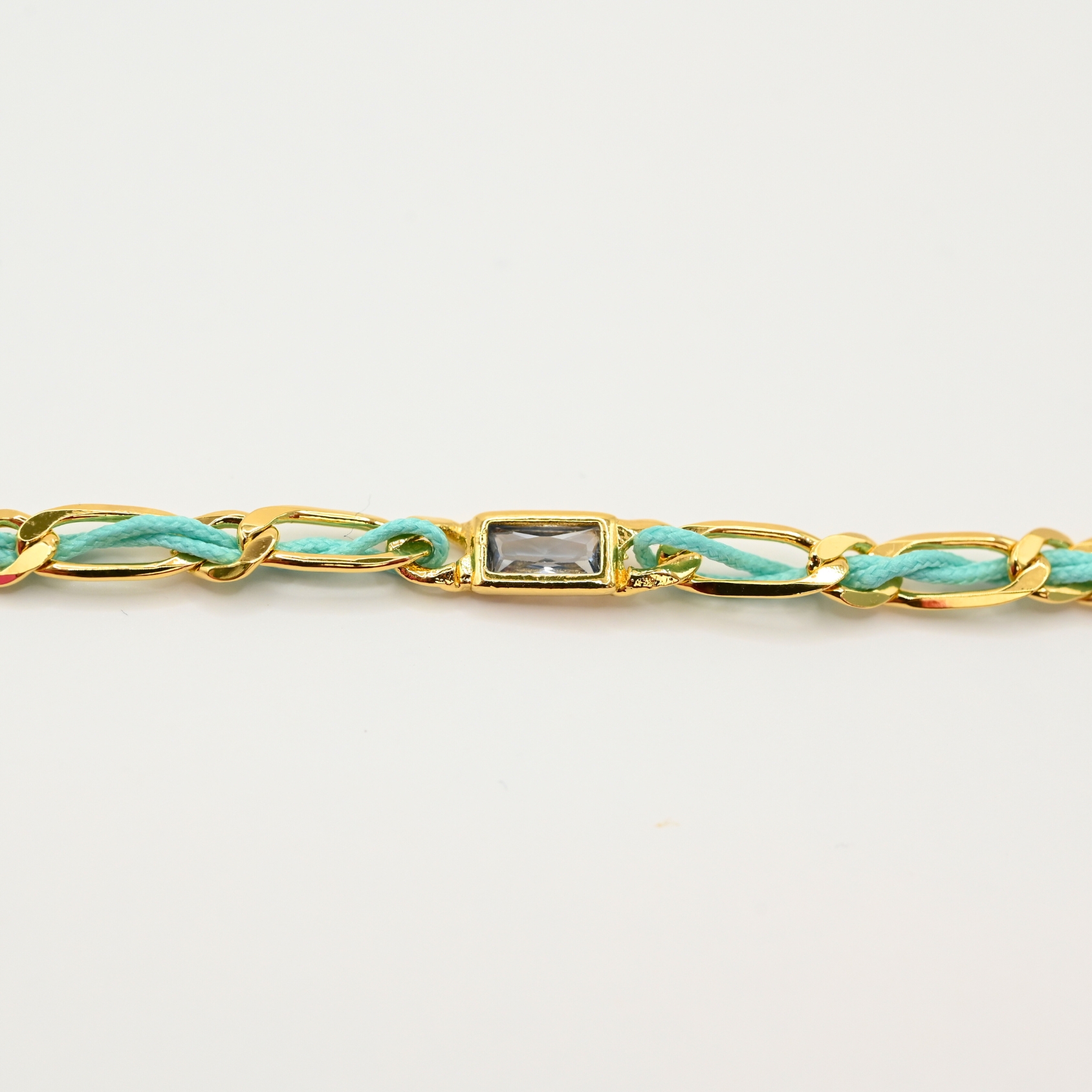 "Bracelet avec un cordon doré et un gemme transparent en son centre. Composition : 100% plaqué or. Contient 1 strass coloré transparent. . Bijou seul, Crédit GEMITY"