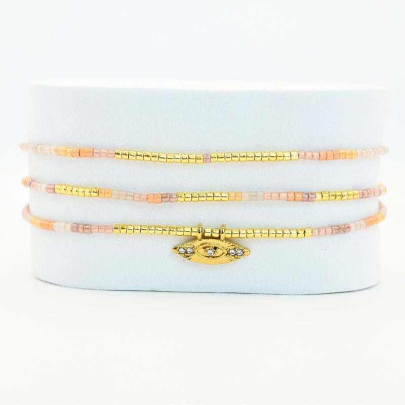 ce bracelet à 3 rangs combine des perles dorées, nude et rose poudré. Le second rang est orné d’un charm œil au centre, ajoutant une touche originale et élégante. . Bijou seul, Crédit GEMITY