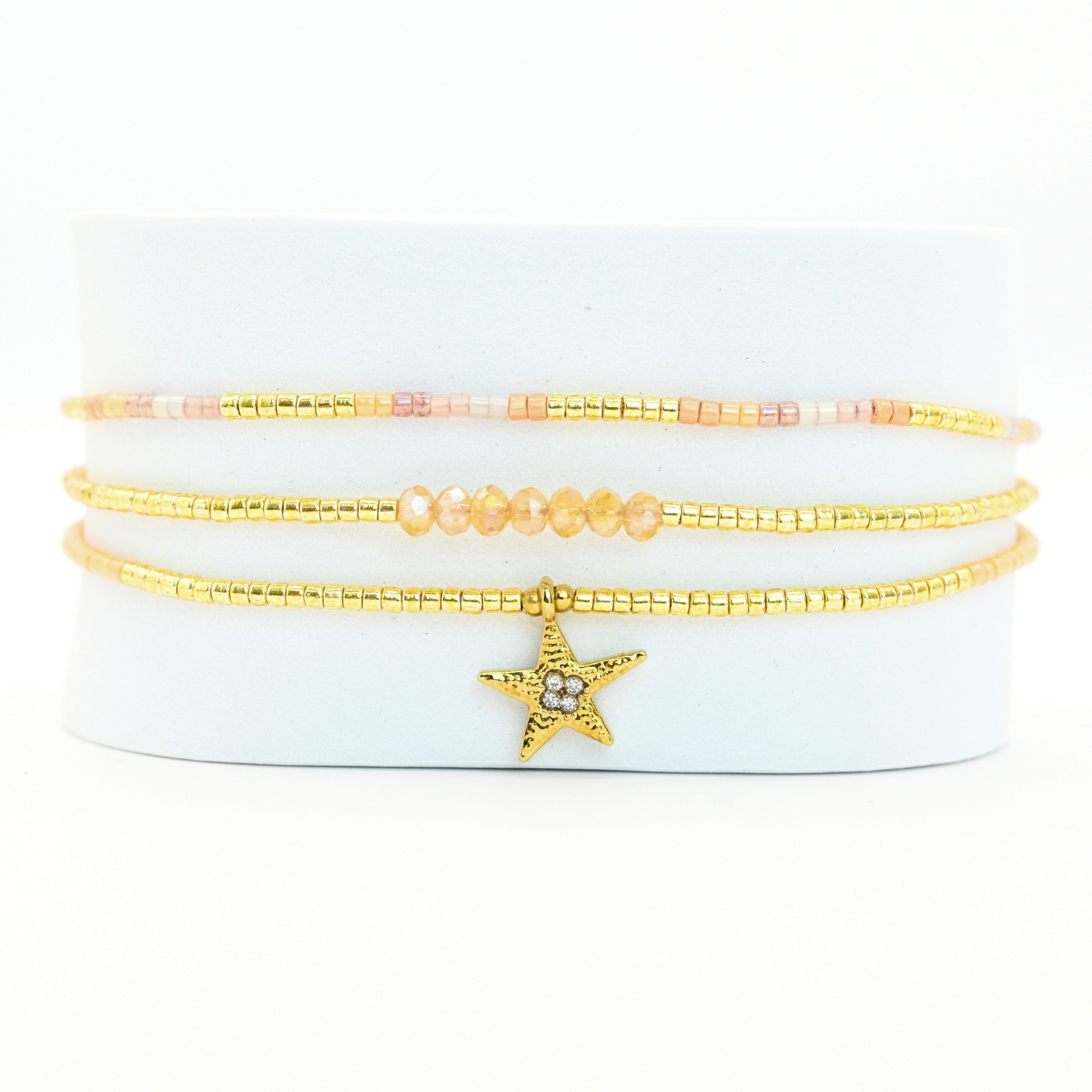 ce bracelet raffiné à 3 rangs combine des perles dorées et nude pour un look élégant et féminin. Le premier rang est orné de perles délicates, tandis que le second présente des perles plus grosses, créant un effet visuel dynamique. Le troisième rang se distingue par un charm étoile au centre, ajoutant une touche de magie et de sophistication. . Bijou seul, Crédit GEMITY