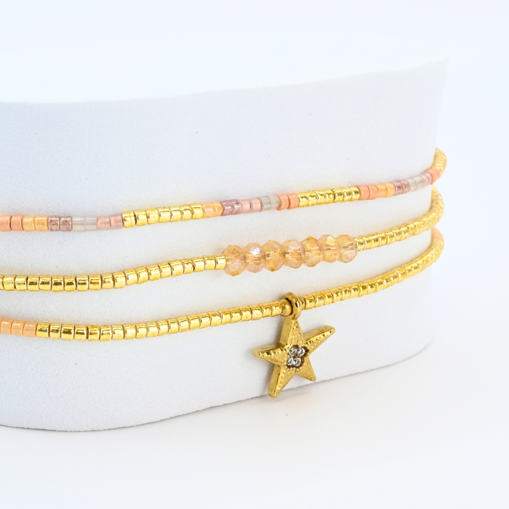ce bracelet raffiné à 3 rangs combine des perles dorées et nude pour un look élégant et féminin. Le premier rang est orné de perles délicates, tandis que le second présente des perles plus grosses, créant un effet visuel dynamique. Le troisième rang se distingue par un charm étoile au centre, ajoutant une touche de magie et de sophistication. . Bijou seul, Crédit GEMITY
