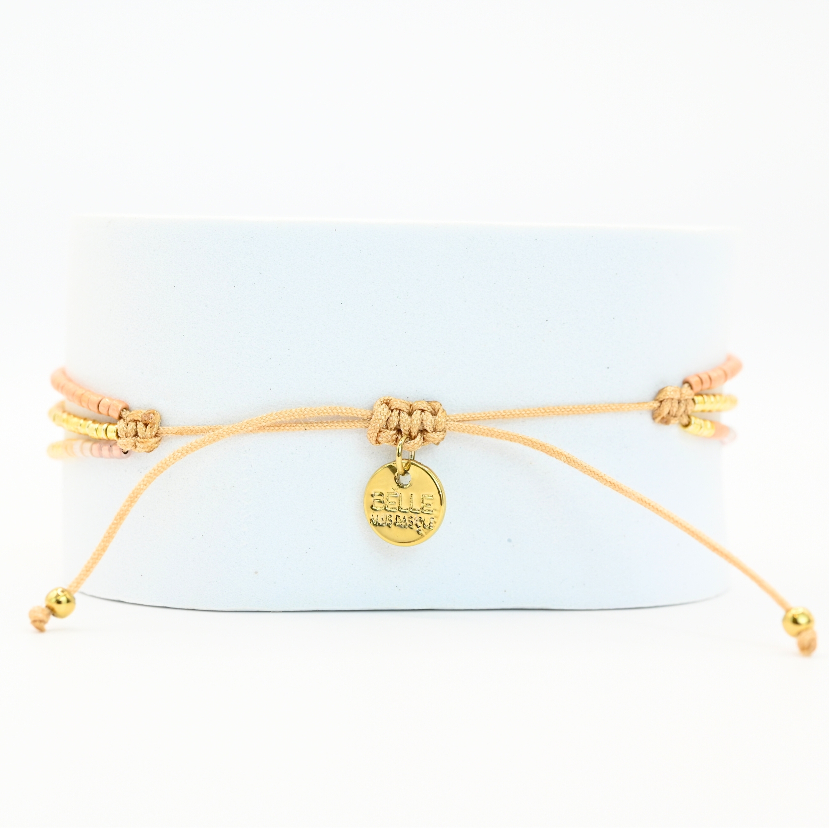 ce bracelet fin à 3 rangs combine des perles dorées, nude et roses, créant une harmonie de couleurs douce et élégante. Le charm rond à strass, placé au centre, ajoute une touche scintillante et raffinée. . Bijou seul, Crédit GEMITY