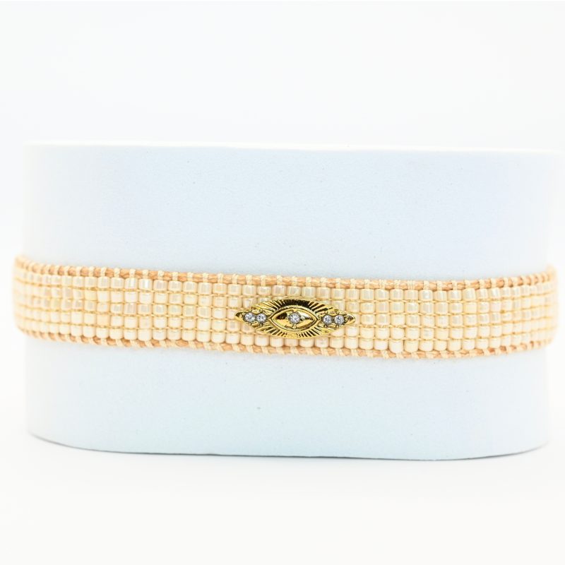 cette petite manchette raffinée se compose de 5 rangs de perles blanches, offrant une touche lumineuse et élégante. Son ornement central en forme d'œil apporte une symbolique protectrice et tendance. . Bijou seul, Crédit GEMITY