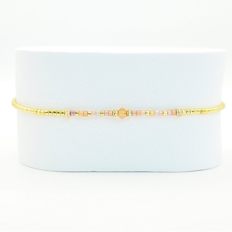 ce bracelet fin et délicat joue sur l’harmonie des couleurs avec son cordon ajustable, ses perles dorées et ses perles dans les tons roses placées en son centre. . Bijou seul, Crédit GEMITY