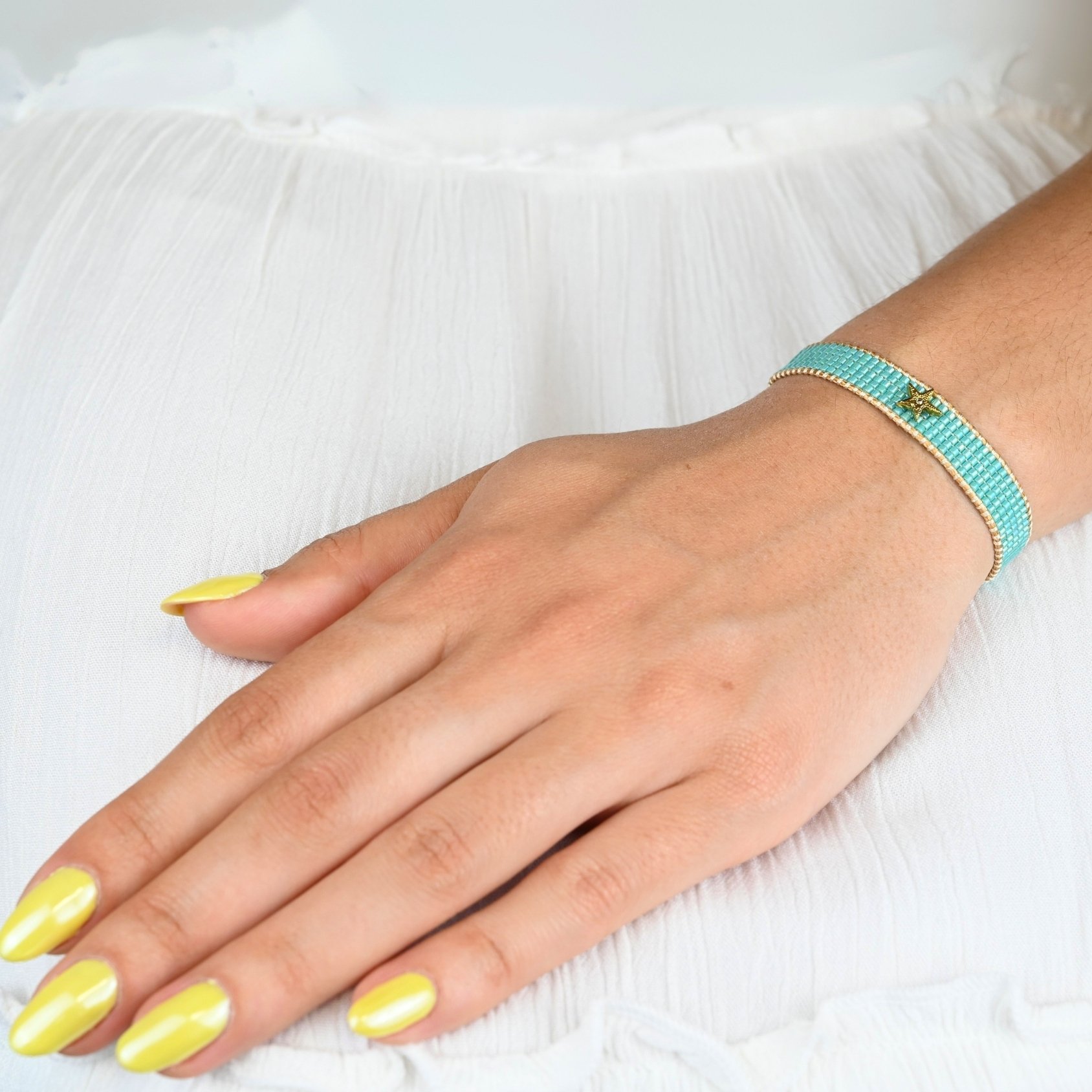 inspirée des nuances apaisantes de l’océan, cette petite manchette se compose de 5 rangs de perles bleues lagon. Son ornement étoile avec un zircon disposé au centre du bracelet apporte une touche lumineuse. . Bijou porté, Crédit GEMITY.
