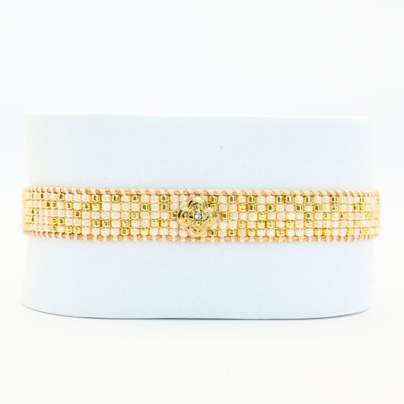 cette petite manchette délicate se compose de 5 rangs de perles nude et dorées, apportant une touche douce et lumineuse à votre poignet. Son ornement central en forme de lotus doré symbolise l’harmonie et la sérénité. . Bijou seul, Crédit GEMITY