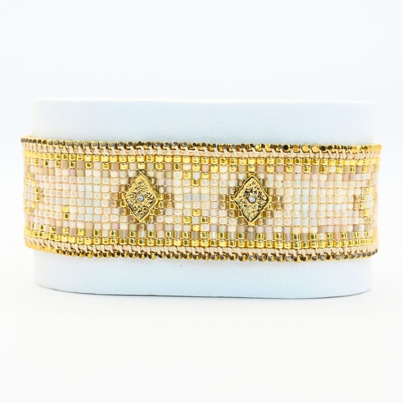 sublimez votre poignet avec cette grande manchette composée de 12 rangs de perles dorées et nude, créant un contraste élégant et lumineux. Deux ornements losange, placés au centre et à chaque extrémité, ajoutent une touche géométrique moderne et raffinée. Bijou seul, Crédit GEMITY