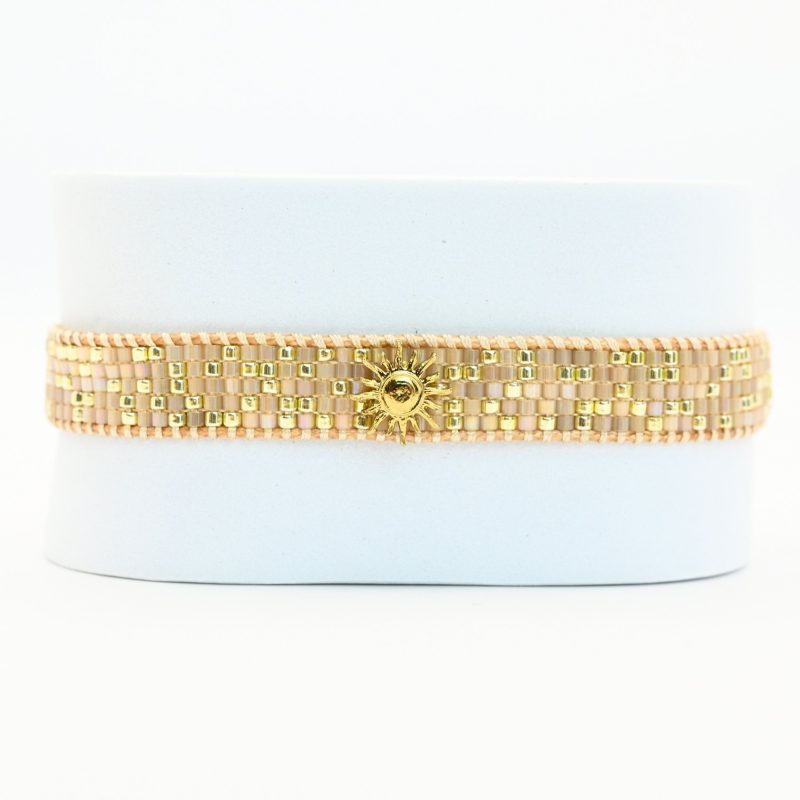 apportez une touche de luminosité à votre poignet avec cette petite manchette élégante. Composée de 5 rangs de perles dorées et nude, elle crée un contraste subtil et raffiné. L'ornement soleil au centre ajoute une note chaleureuse et scintillante, évoquant l’éclat du jour.. Bijou seul, Crédit GEMITY