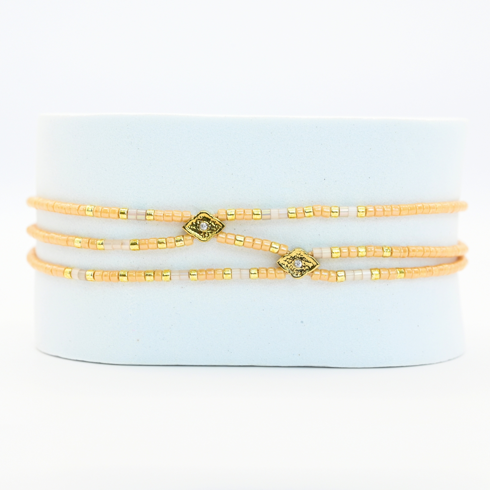 ce bracelet fin à 3 rangs associe des perles dorées et nude, créant un look élégant et discret. Les rangs sont réunis par deux ornements délicats, ajoutant une touche supplémentaire de raffinement et de structure. . Bijou seul, Crédit GEMITY