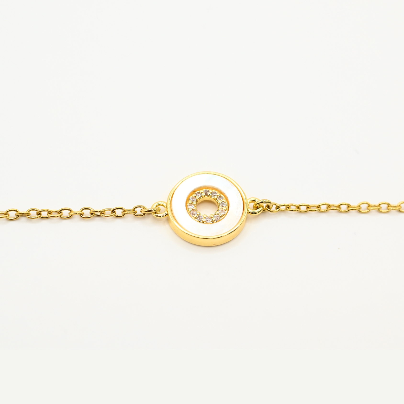 "Ce bracelet de 15 cm est en acier inoxydable et ajustable avec sa chaîne d’extension de 4 cm. Le motif central est de 1 cm et il est en nacre cerclée de métal et de zirconium. Ce bijou est doré à l’or fin 24 carats et il ne provoque pas d’allergies dues au nickel. . Bijou seul, Crédit GEMITY"