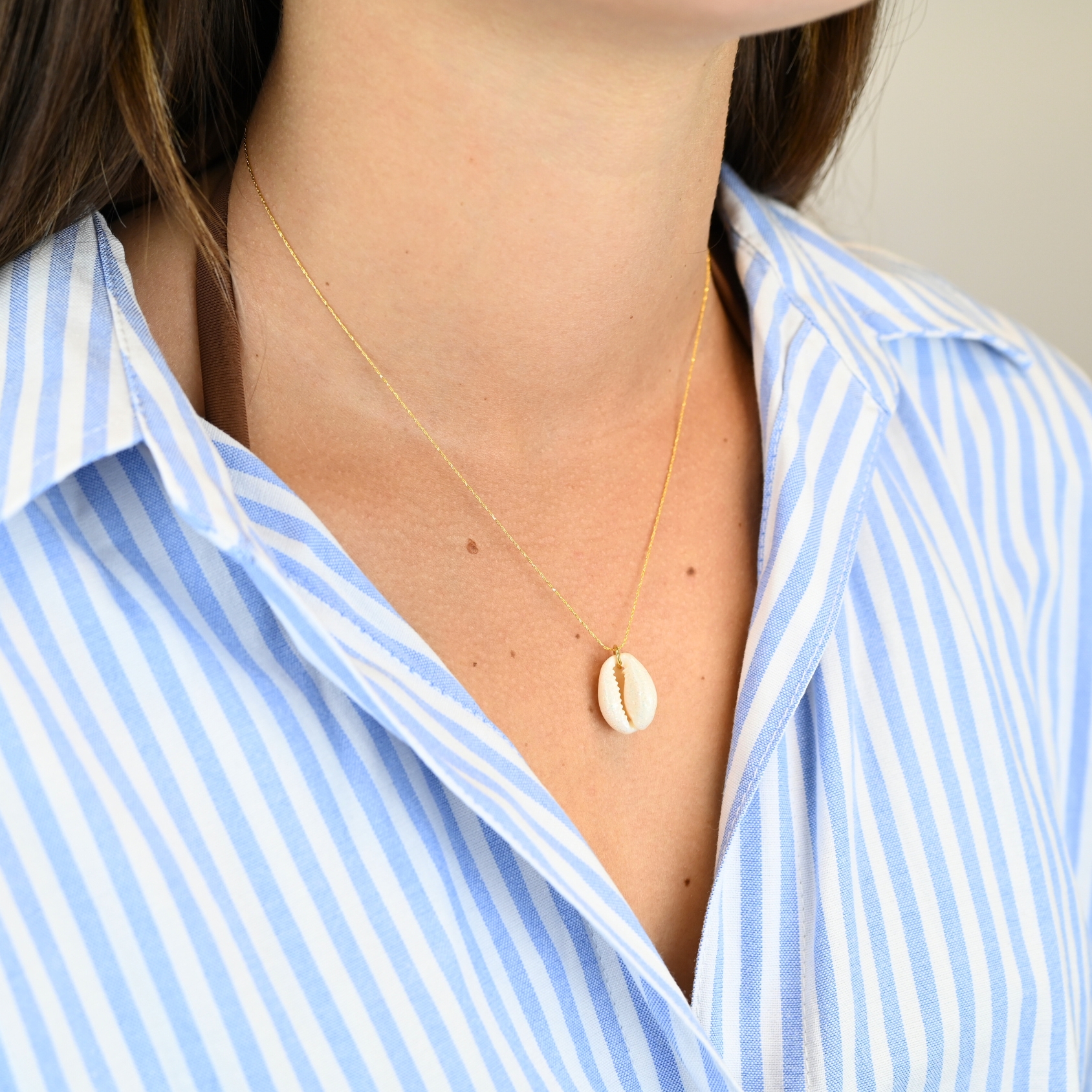 "Collier plaqué or (3 microns) coquillage émaillé Véritable cauri (coquillage) d’une longueur d’environ 2 cm Taille de la chaîne : 39 cm (+5cm de chaîne de rappel) . Bijou porté, Crédit GEMITY."