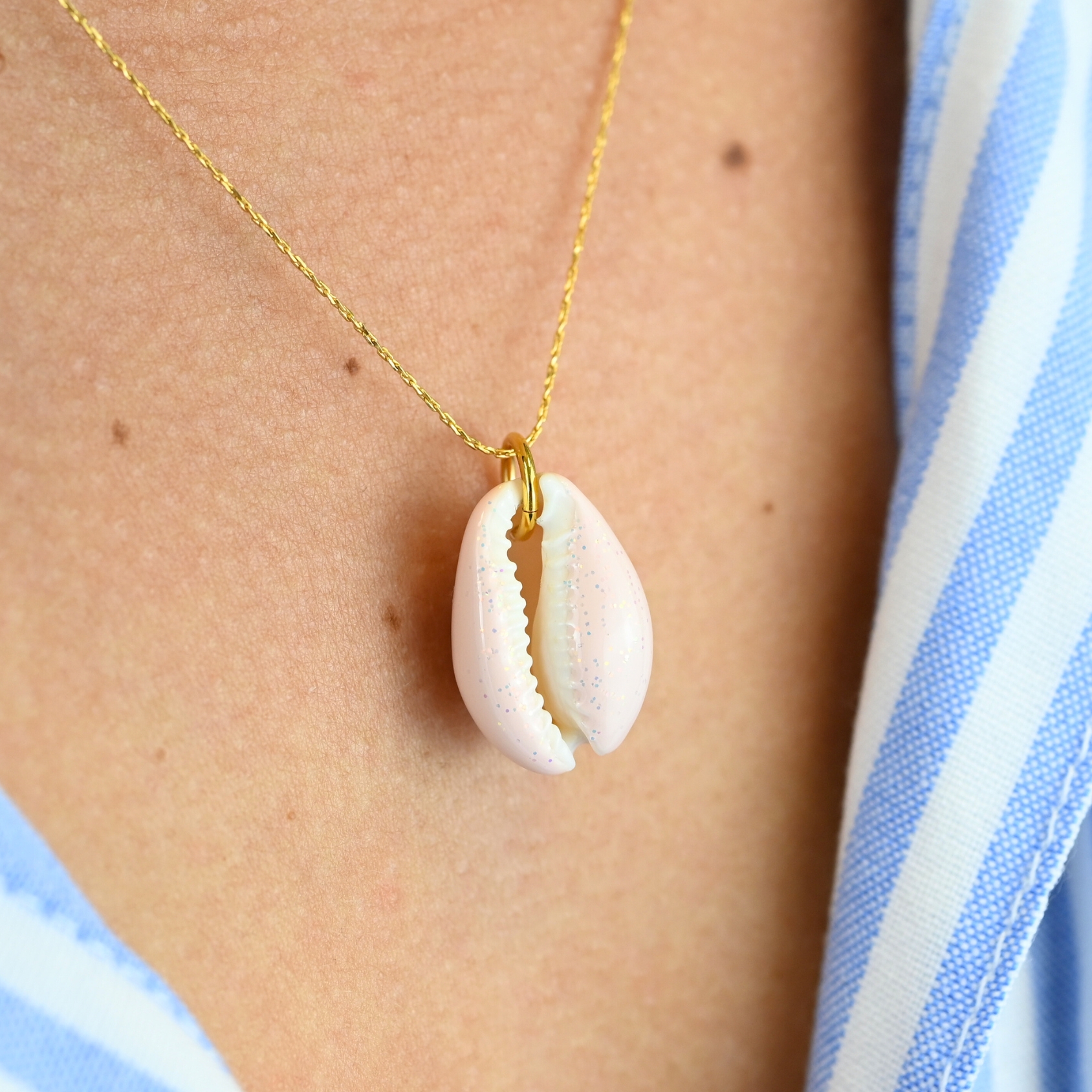"Collier plaqué or (3 microns) coquillage émaillé Véritable cauri (coquillage) d’une longueur d’environ 2 cm Taille de la chaîne : 39 cm (+5cm de chaîne de rappel) . Bijou porté, Crédit GEMITY."