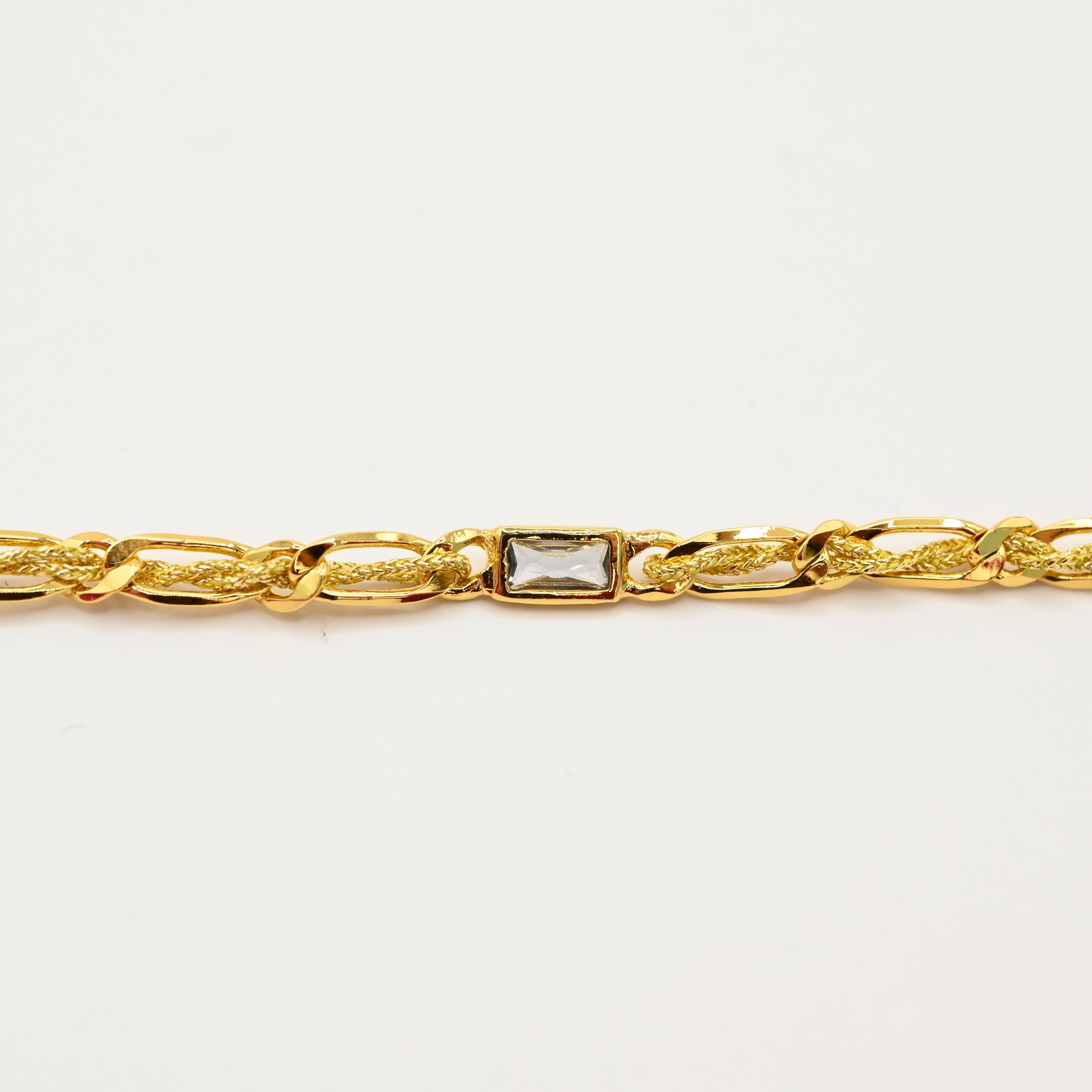 "Bracelet avec un cordon doré et un gemme transparent en son centre. Composition : 100% plaqué or. Contient 1 strass coloré transparent. . Bijou seul, Crédit GEMITY"