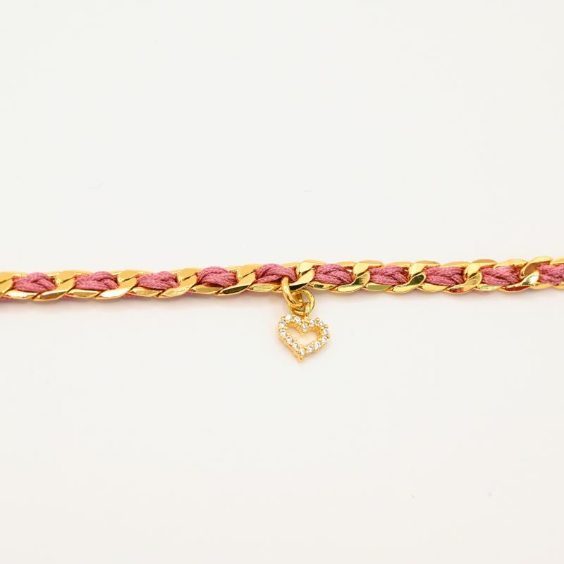 "1 pampille coeur strass Couleur tressage : rose poudré. Fermoir réglable. Matière : plaqué or et incrustation de fils de coton polyester tressés. Utilisation possible sous la douche ! . Bijou seul, Crédit GEMITY"